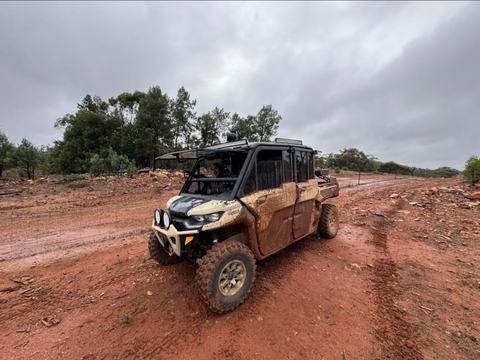 Muddy Can-Am utility vehicle on a red dirt track